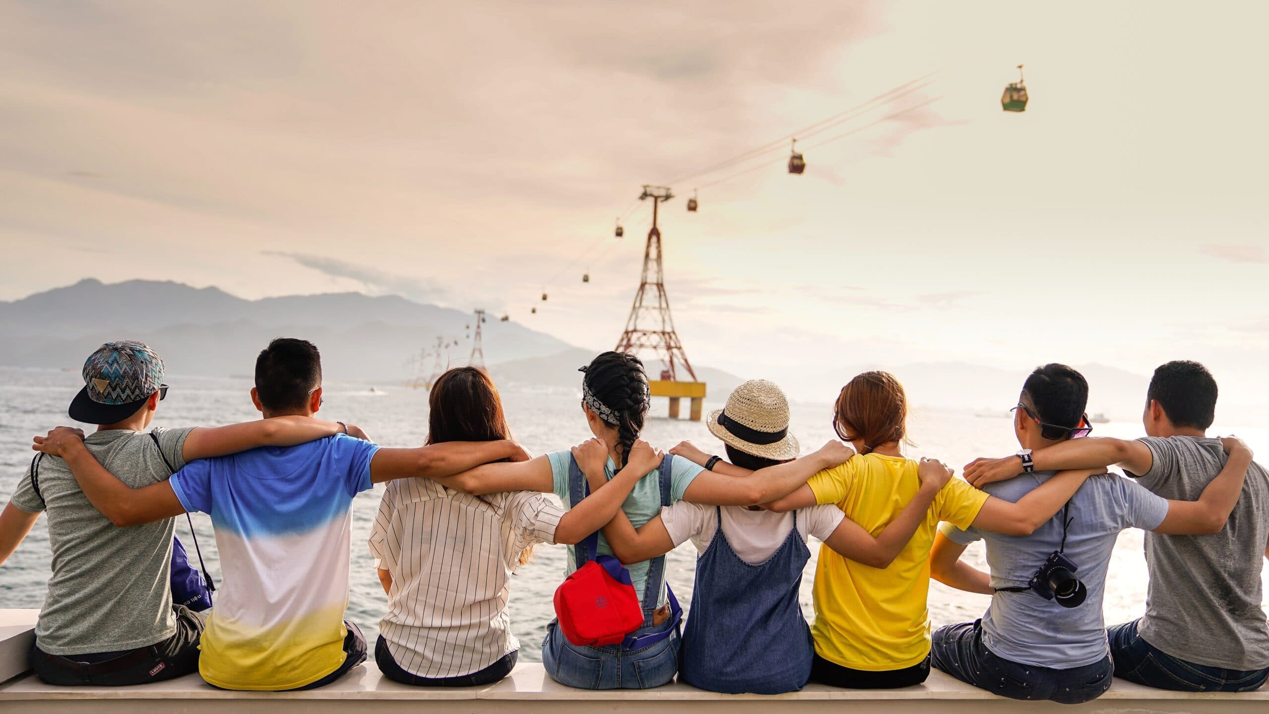 A group of people sit with their arms around each other, looking at a sunset.